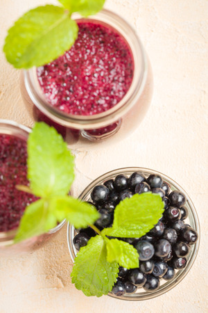 Blueberry smoothie close up photography - top view of summer blended vitamin cocktail decorated with fresh green mint leaves and raw ripe berries on yellow pastel background for healthy food concept.の写真素材