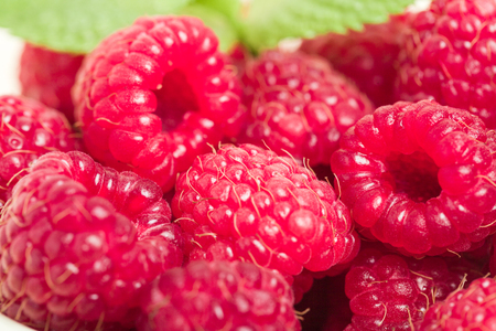 Ripe raspberries with green mint leaves - close up macro photography of summer seasonal raw berries...