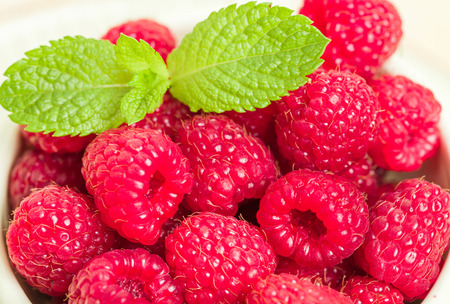Ripe raspberries with green mint leaves - close up macro photography of summer seasonal raw berries...