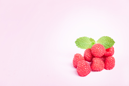 Raw ripe raspberries with fresh green mint leaf isolated on pink pastel background. Close up...