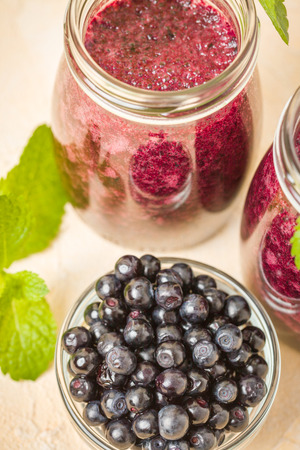 Blueberry smoothie decorated with fresh green mint leaves and raw ripe berries on yellow pastel background - transparent jars of summer blended vitamin cocktail with copy space.の写真素材