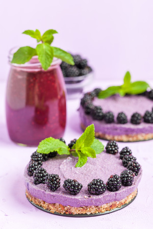 Raw blackberry dessert decorated with fresh ripe forest berries and green mint leaves and blended smoothie on pastel violet background - sweet organic food for healthy eating and dieting concept.の写真素材