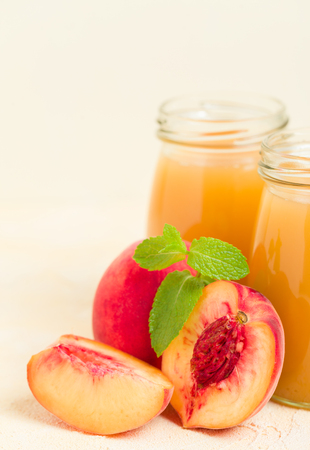 Peach smoothie in glass jars with fresh ripe fruits and green mint leaves on yellow pastel background - raw sweet dessert or breakfast drink for healthy organic eating concept.の写真素材