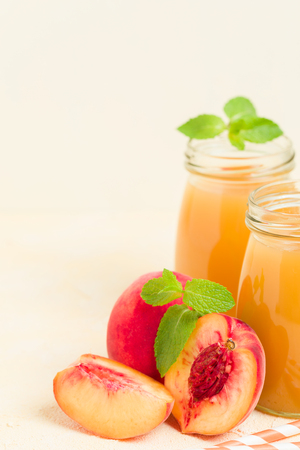 Peach smoothie in glass jars with fresh ripe fruits and green mint leaves on yellow pastel background - raw sweet dessert or breakfast drink for healthy organic eating concept.の写真素材