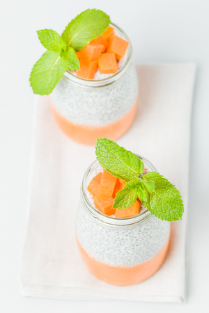 Chia seeds pudding with pumpkin puree in beautiful glasses with green mint leaves and cut fresh ripe orange vegetable on light gray background - raw vegetarian sweet organic dessert.の写真素材