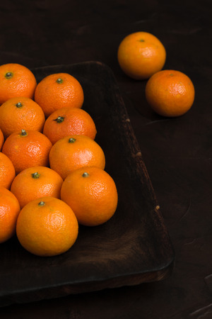 Fresh ripe mandarin orange on wooden board on blackの写真素材