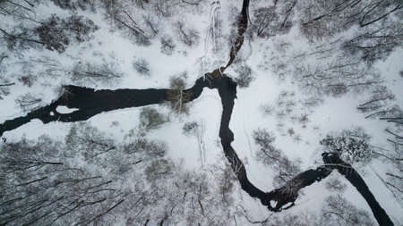 Aerial winter landscape. Tiny river between snowy forestの写真素材