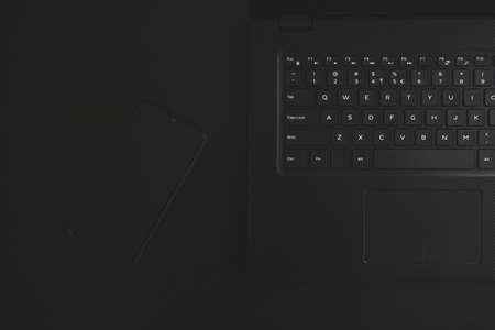 Black Laptop and black smartphone on black table. Dark theme. Top view