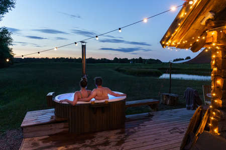Young couple enjoy outside ofuro japanese hot tub in romantic environment. Idyllic bathtub in darkの写真素材