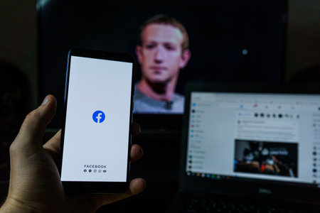 Facebook applicaton and logo in background. Mark Zuckerberg on screenのeditorial素材
