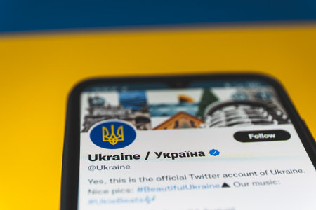 Russia and Ukraine war. Ukraine twitter account on smartphone. Ukraine flag in backgroundのeditorial素材