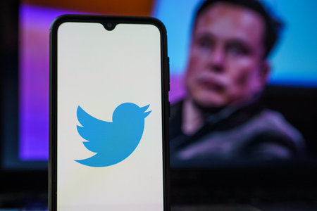 Twitter logo on smartphone and Elon Musk in the background. Elon Musk joins Twitter boardのeditorial素材