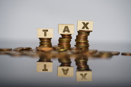 Tax on wooden blocks on stacked coins. Visual concept of growing taxes. High quality photo
