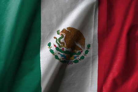 Mexican flag with vertical green, white, and red stripes, featuring the national coat of arms an eagle holding a serpent in its beak and talon, perched on a cactus in the center.の写真素材