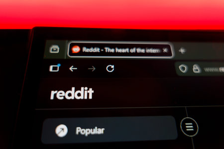 Close up of a computer screen showing the Reddit homepage with the official logo, browser tab, and navigation menu under a vibrant red light, representing online communities and social media forums.のeditorial素材