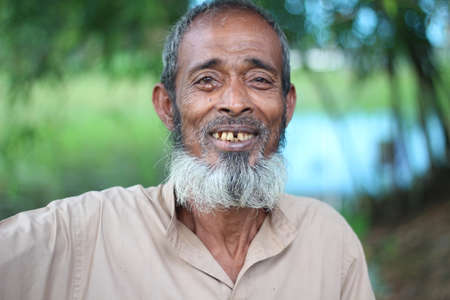 Bangladesh, Rangpur- July 03, 2021. An old man is standing and smiling his behind natureのeditorial素材