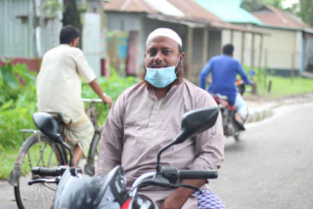 Bangladesh, Rangpur- July 03, 2021. An old man is sitting on a motorbike on the street wear a mask in the COVID-19 situationのeditorial素材