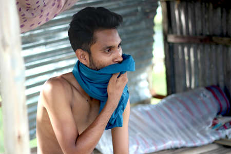 Bangladesh, Rangpur- July 12, 2021. A boy covers his face with his blue t-shirtのeditorial素材
