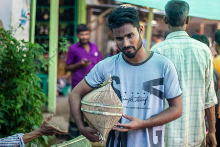 Bangladesh, Rangpur- August 31, 2021. A young boy stands in the market with a fishing trap made of bamboo and his behind background blur.のeditorial素材