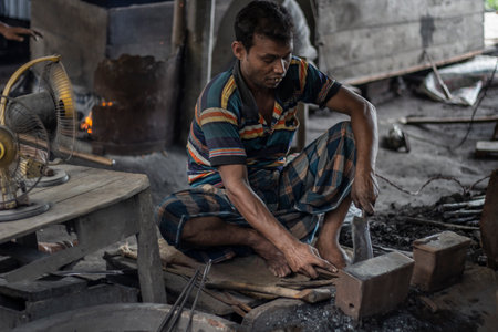Bangladesh, Rangpur- August 31, 2021. An old poor man is sitting in a temporary iron shop in the local market and making all kinds of daily necessities iron, steel products, and the background blurのeditorial素材