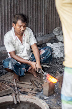 Bangladesh, Rangpur- August 31, 2021. An old poor man is sitting in a temporary iron shop in the local market and making all kinds of daily necessities iron, steel products, and the background blurのeditorial素材