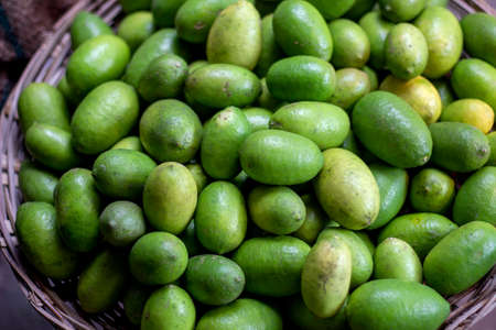 Many lemons are put in a bamboo basket and their color is green and background blur