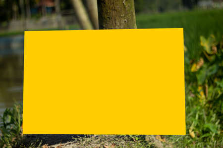 A yellow sign board is leaning against a tree on the ground and the background blur behind it.の写真素材