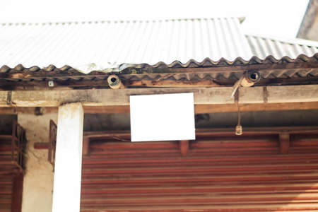 In front of a house hangs a small white blank signboard with wood and its background is blurredの写真素材