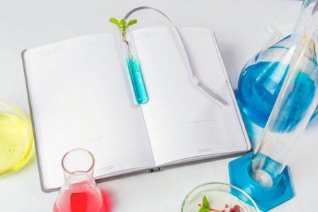 test tube with leaves on a laptop which lies on a white table. Nearby are flasks with colored liquids. Backgraund.の写真素材