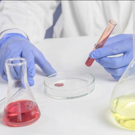 Laboratory work, male hands holding a test tube, in blue rubber gloves, a blood test. Close up.