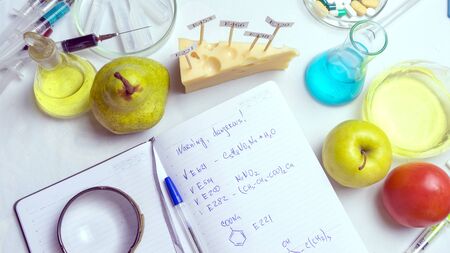 Food safety laboratory procedure, analysing fruits from the market. Notebook and blue pen on the lab table. In the cheese are signs with the code E-supplements. top viewの写真素材