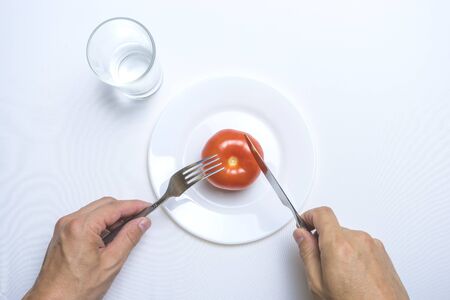 male hands holding fork and knife on a plate with tomato on white table.の写真素材