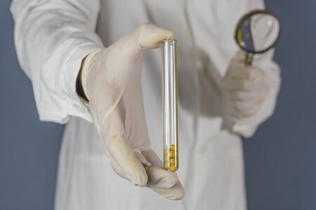 The researcher holds a test tube with soybeans and a magnifier. GMO concept. Selective focus.