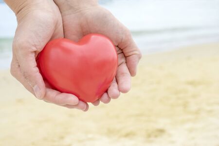 Red fabric heart lay on palm of hand with sea on background. Valentine day.の写真素材