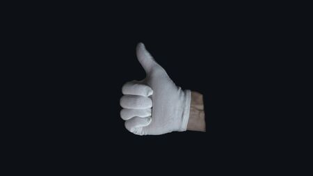 White-gloved hand on a black background. hand in white glove showing sign - thumb up, on black background, sign languageの写真素材