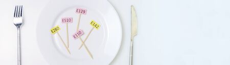 Photo Harmful food additives. Knives, fork, plate. On the plate there are several tables with the E-supplement code. Copy spaceの写真素材