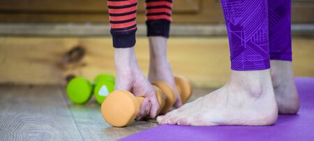 Photo teenage girl holds yellow dumbbells with her hands. The concept of a healthy lifestyle, sport and home workout.の写真素材