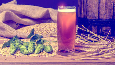 Beer. Still life with Vintage beer barrel and glass light beer. Fresh amber beer concept. Green hop and gold barley on wooden table. Ingredients for brewery. Brewing traditionsの写真素材
