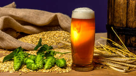 Still life with Vintage beer barrel and glass light beer. Fresh amber beer concept. Green hop and gold barley on wooden table. Ingredients for brewery. Brewing traditionsの写真素材