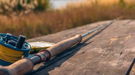 Fly fishing rod with on wood background. Autumn sunny day.