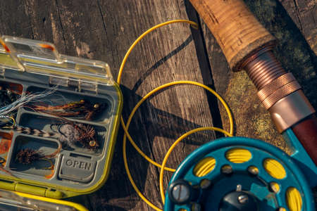 Fly fishing rod with on wood background. Fly fishing gear, which includes a reel and containers of...