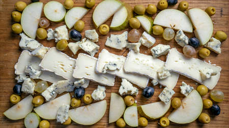 Photo Sliced green pears, slices of white soft brie cheese, olives and grapes on a wooden board....