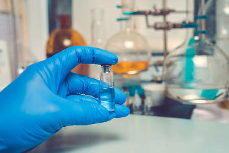 Photo Transparent vial or bottle with the vaccine is in the doctor's hand, which is dressed in blue medical gloves. The concept of vaccination, research or production of vaccines against various diseasesの写真素材