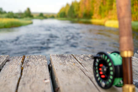 A fly fishing rod and reel on the river bank. Background river.の写真素材