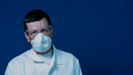 Photo Chemistry laboratory assistant in goggles and a mask. Portrait, blue background.の写真素材