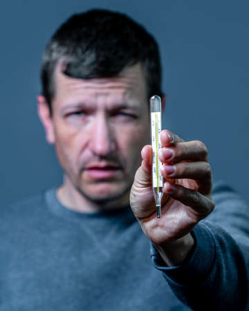 Portrait A young man fell ill and holds a thermometer in his hand.