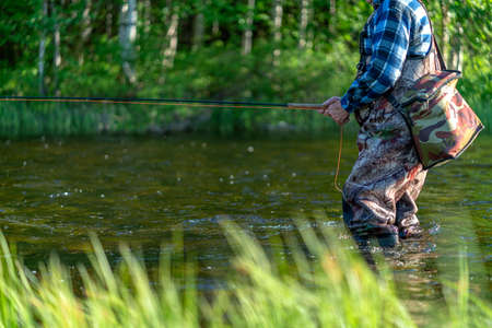 A fisherman in a mountain river catches trout, morning. side viewの写真素材
