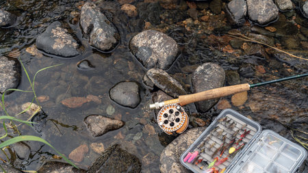 A fly fishing rod and an open fly fishing box lie on the rocks of a mountain river. top viewの写真素材