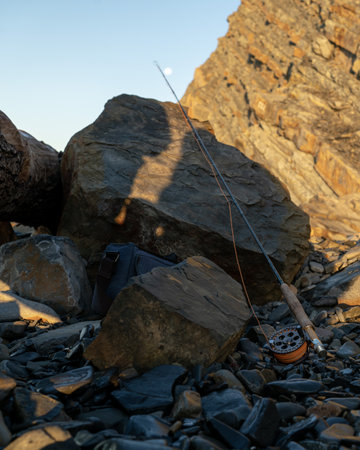 A fly fishing rod on the sea rocks at sunsetの写真素材