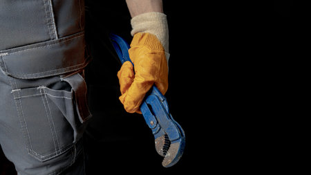 A man's hand holds an adjustable wrench on a black background. Place to place text